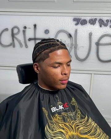 Client in cornrows with a fresh taper and lineup, seated in front of the CRITIQUE wall